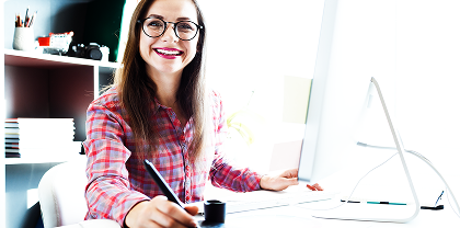 Graphic designer working at a desk, using a pen tablet to draw on a digital design while seated in a modern office workspace.